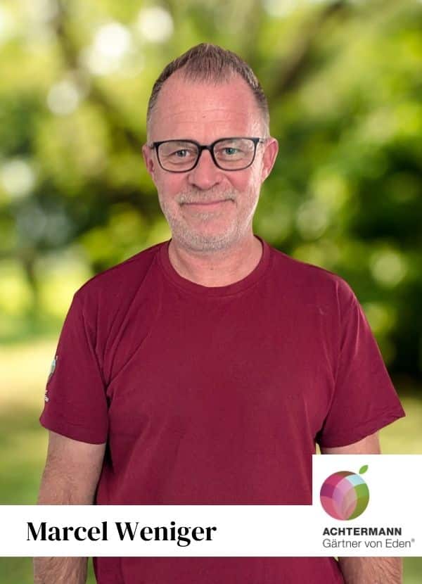 Marcel Weniger im Porträt, Achtermann Gärtner von Eden Mann mit grauen Haaren, trägt einen roten Hoodie und steht aufrecht mit neutralem Ausdruck.