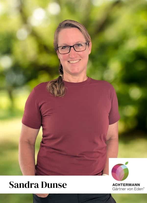 Sandra Dunse, Porträt im Garten mit Achtermann-Gärtnerlogo Porträt von Julian Schölzel in einem roten T-Shirt vor unscharfem Hintergrund.